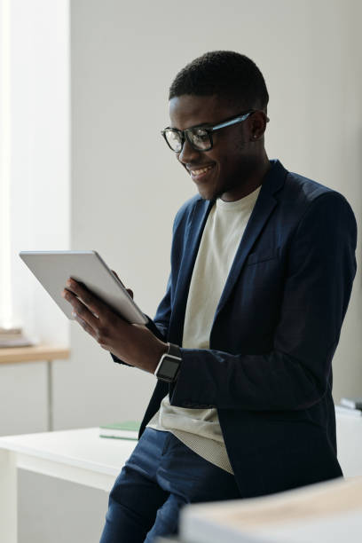 istock Young smiling male manager in eyeglasses and formalwear using tablet 1496638864