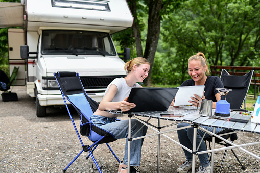 Smiling Female Stock Market Workers Comparing Results Outside RV While Enjoying Camping Trip