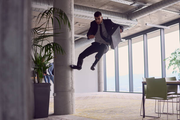 en la oficina moderna, un hombre de negocios con un maletín cautiva a todos mientras realiza emocionantes acrobacias aéreas, desafiando la gravedad con sus atrevidos saltos y mostrando su agilidad con un espectáculo impresionante. - showmanship fotografías e imágenes de stock