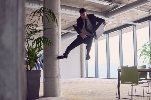 現代のオフィスでは、ブリーフケースを持ったビジネスマンがスリリングな空中アクロバットを実行し、大胆な跳躍で重力に逆らい、息を呑むようなショーマンシップで敏捷性を披露しなが� - showmanship ストックフォトと画像