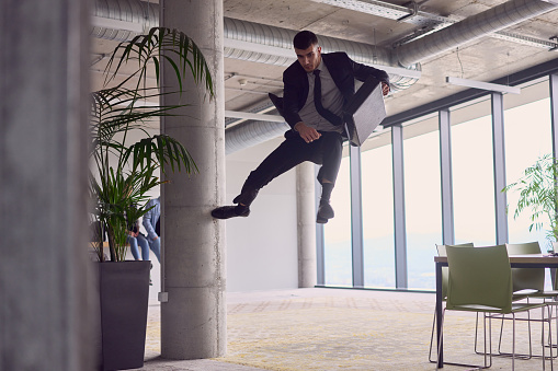In the modern office, a businessman with a briefcase captivates everyone as he performs thrilling aerial acrobatics, defying gravity with his daring leaps and showcasing his agility with breathtaking showmanship