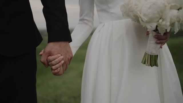 Groom and bride are holding hands. Happy wedding couple video. Romantic relationship. White dress. Close up, slow motion.