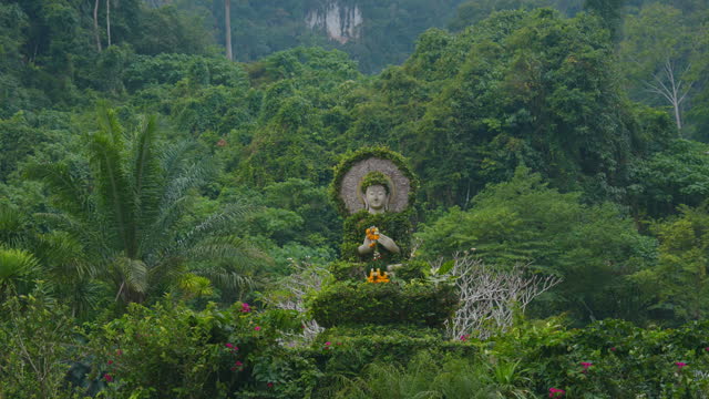 Sculpture of Buddha covered in greenery in the middle of the jungles