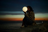 young lady playing with a moon shaped artificial lamp outdoors