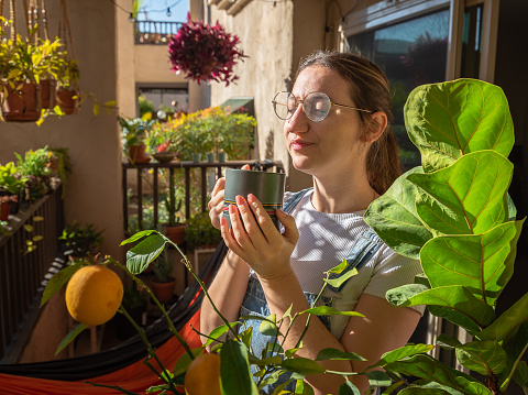 Woman enjoying her coffee on her sunny balcony surrounded by plants and lemons in California