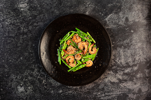 Stir-fried shrimp asparagus teriyaki on a plate on a black slate background top view, healthy food concept.
