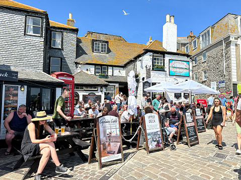 Crowd of people sitting by Sloop inn and drinking ale and beer. The Sloop Inn on the busy quayside with tourists and holidaymakers.