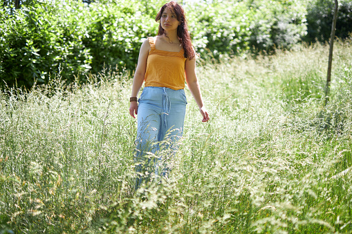 girl in blue jeans and orange shirt walking around forest
