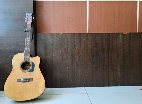 istock A brown acoustic guitar is leaning against a wall with a texture resembling wood. 1496670012
