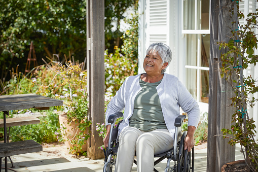 Happy senior woman sitting in her wheelchair outside in the garden