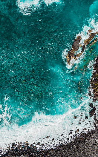 Stones among turquoise waves and sea foam from above. Atlantic ocean coastline with rocks. Madeira island, Portugal. Aerial drone photography. Beautiful landscape. Scenery outdoor background.
