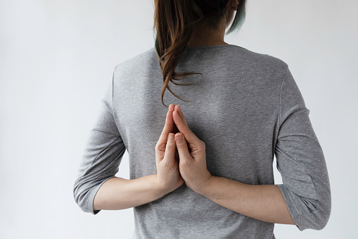 Unrecognizable caucasian female is doing Reverse Anjali Mudra in front of white background. Meditation and yoga concept.