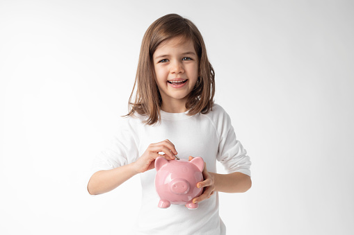 Little girl with piggy bank  wearing white in front of white background.