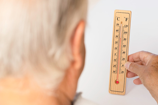 Over the shoulder view of senior man holding thermometer in hand showing high temperatures in front of white background.