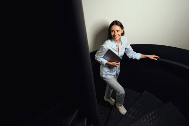 istock Smiling female with her laptop climbing spiral staircase 1496678288