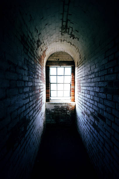 istock Spooky narrow old brick corridor with light shining through a window at the end 1496686695