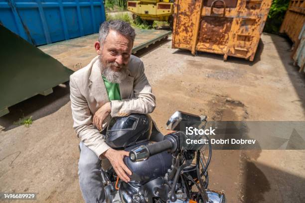 A Mature Man Wearing A Light Green Tshirt A Beige Jacket And Gray Jeans On A Bobber Motorcycle Stock Photo - Download Image Now