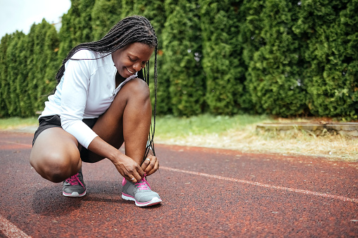 Young athlete woman tie shoelaces before running on running track.