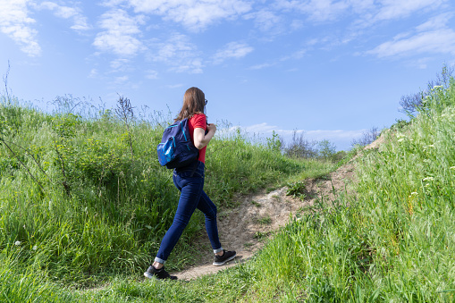 Tourist woman with backpack walking in deciduous forest. Active adult leisure of hiking in green valley. Person enjoy wanderlust and view of the spring grassy hill. Female hiker explore of wildlife.