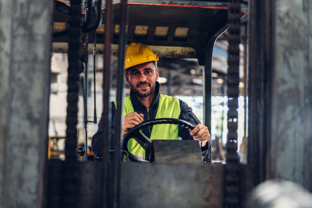 istock Man worker at forklift driver happy working in industry factory logistic ship. Man forklift driver in warehouse area. Forklift driver sitting in vehicle in warehouse 1496703134