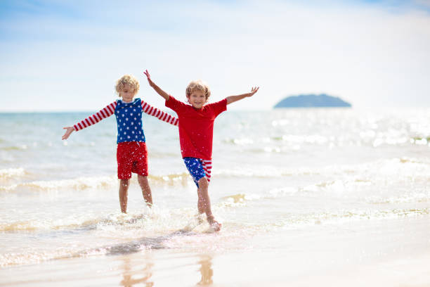 Kids run with USA flag on sunny beach. 4th of July celebration. American family fun on Independence Day weekend. Patriotic children celebrate US holiday. Boy and girl with symbols of America.