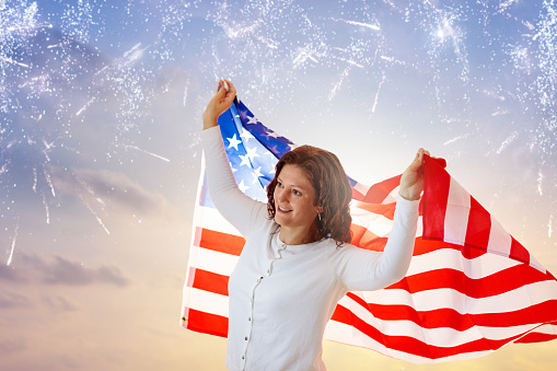 American family celebrating 4th of July. Woman watching Independence Day fireworks holding US flag. Proud USA fans cheer and celebrate. Young woman with America symbol. National holiday party.