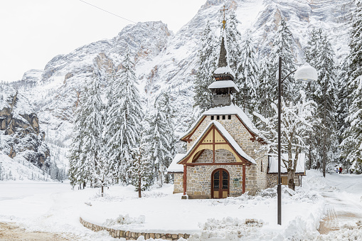 Beautiful view of Chapel by Braies Lake completely iced in a snowy winter day; Alto-Adige, Italy; Dolomites