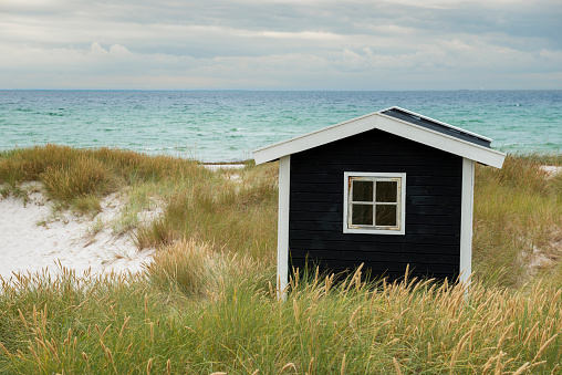 Black Beach hut in the dunes. Skanor/Falsterbo in Skane, Sweden. In the horizon Denmark, a tanker and a sailboat is visible.