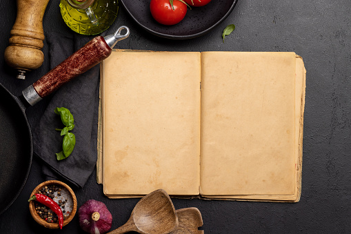 Top-down view of a kitchen table with ingredients, utensils, and an open cookbook with empty pages, perfect for creating a mockup for recipes or menus