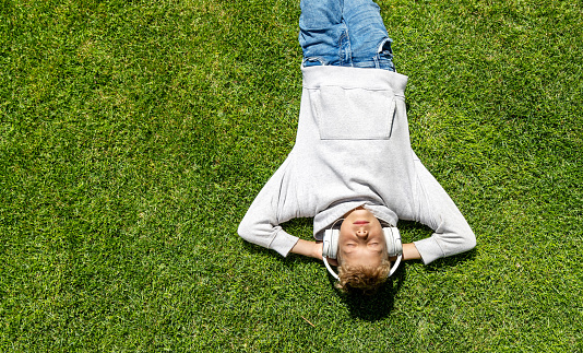 A boy relaxing on grass, listening to music with headphones. Flat lay