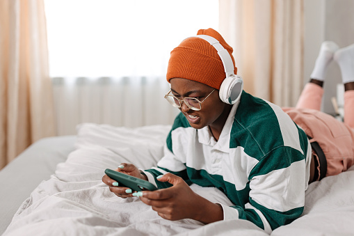 A young African American woman with eyeglasses using headphones and mobile phone to watch a movie