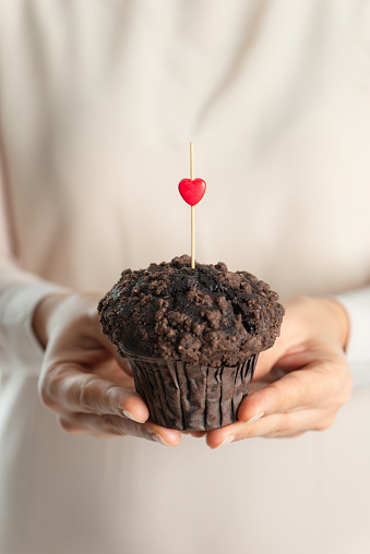 Unrecognizable female is holding a muffin with one stick and a small red heart shape on it.