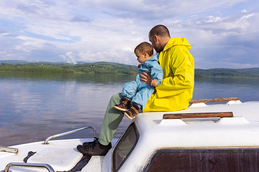 A man and his young son sit peacefully on a small boat, surrounded by the tranquil waters of the lake.