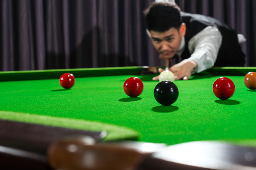 Asian man playing snooker, snooker club, Asian man playing snooker with selective focus on snooker ball and snooker ball movement.