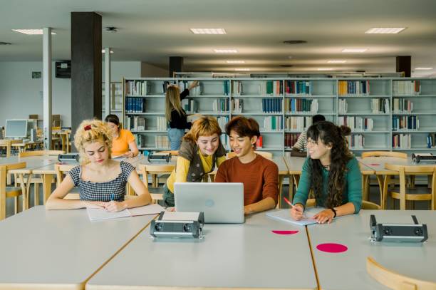 istock Group of multiethnic students discussing in library with laptop 1496724925
