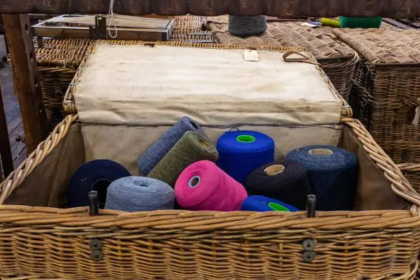 A wooden table displays a variety of colorful yarns in a woven basket
