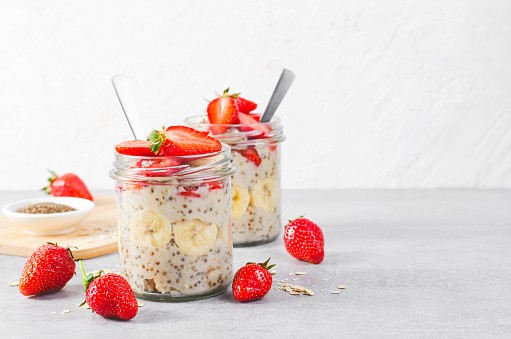 Overnight Oats with Fresh Strawberry, Banana and Chia Seeds in Jars on Grey Background, Healthy Snack or Breakfast