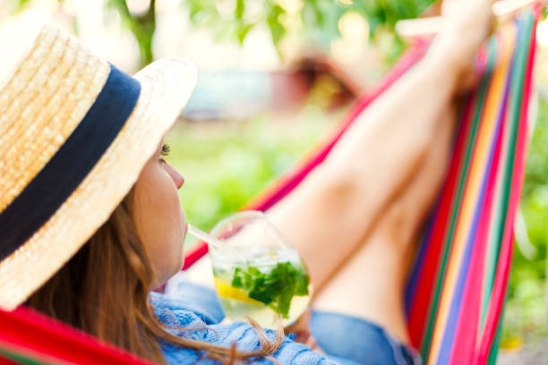 istock Young woman drinking cocktail while lying in comfortable hammock at green garden 1496737310