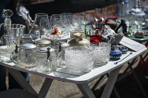 Glass dishes, beer mugs and drinking glasses as well as other tableware on a table at a flea market on a sunny day, selected focus, narrow depth of field