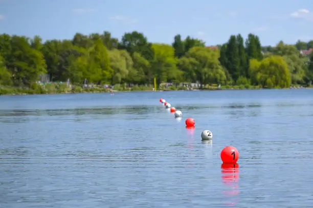 Photo of Floating balls in red and white mark the finish line on the lake during a rowing regatta, copy space, selected focus