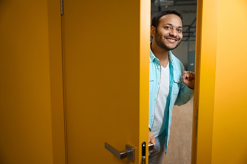 Male in blue shirt standing in the office, opening door and looking at camera