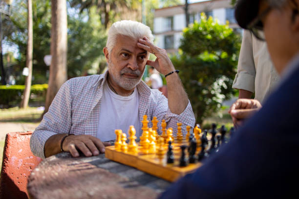istock Three senior Latin friends sitting at the park and playing chess 1496738228