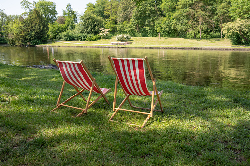 Red and white striped sun loungers standing in the lawn on the natural bank of a river, inviting idyll on a sunny summer day, copy space, selected focus, narrow depth of field