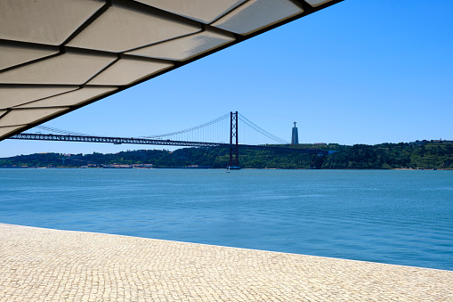 Lisbon, Portugal — June 15, 2018: The MAAT is a cultural project for the city of Lisbon that is focused on three areas: art, architecture and technology. The museum is near the Tagus River and opened in June of 2016. The museum was designed by Welsh architect Amanda Levete. In the background is the Ponte 25 de Abril, a 2km suspension bridge linking Lisbon with Almda.