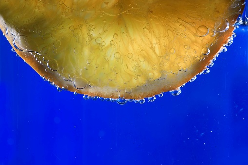 A close-up of a freshly cut orange floating in a bowl of crystal clear water, with air bubbles gently rising to the surface