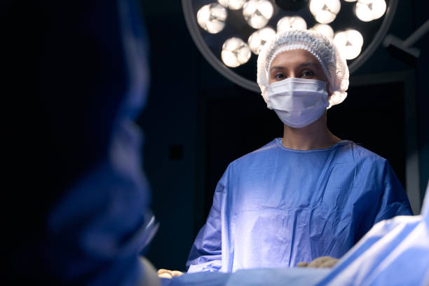 防護マスクと制服を着た女性が手術台に立つ - scrubs surgeon standing uniform ストックフォトと画像