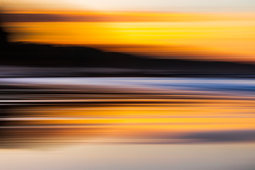 Motion blur pan seascape of light reflecting off waves and wet sand shoreline.