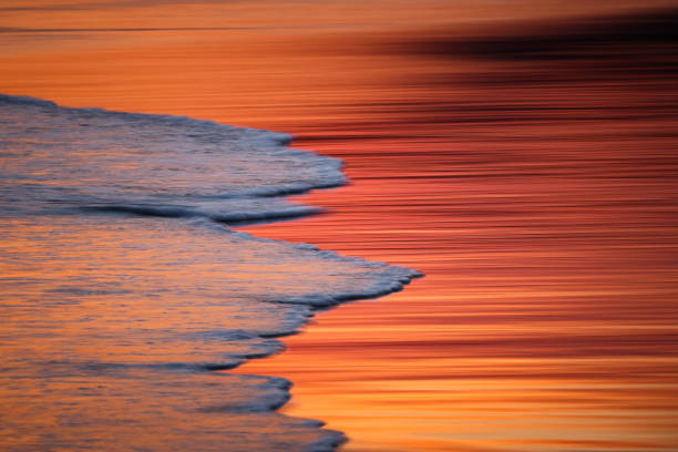 Motion blur capture of tidal surge or ocean waves lapping on beach with golden light reflecting off surface