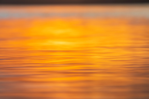 Close up of light reflecting on smooth ocean surface from sun setting.