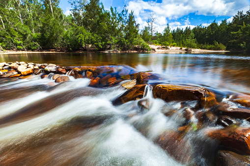 Freshwater stream flowing over rocks in tranquil forest scene. Long exposure.